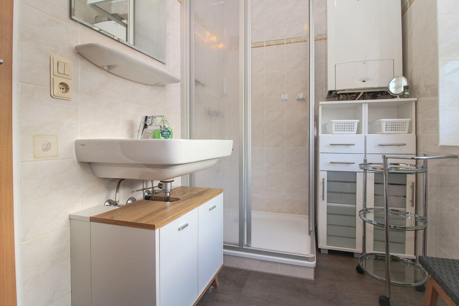 Badezimmer mit Dusche, Waschbecken und Aufbewahrungsmöbel.
