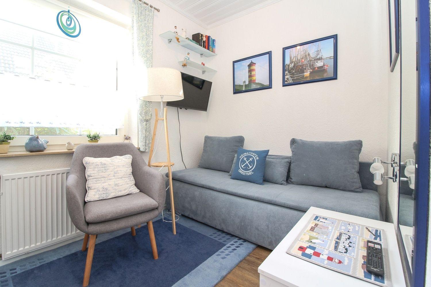 Wohnzimmer mit Sofa, Sessel, Fernseher und Wandbildern.