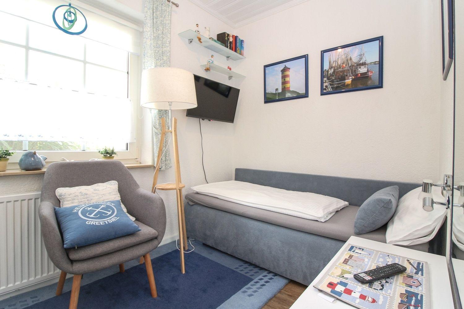 Ein Schlafzimmer mit Sofa-Bett, Sessel und Fernseher an der Wand.