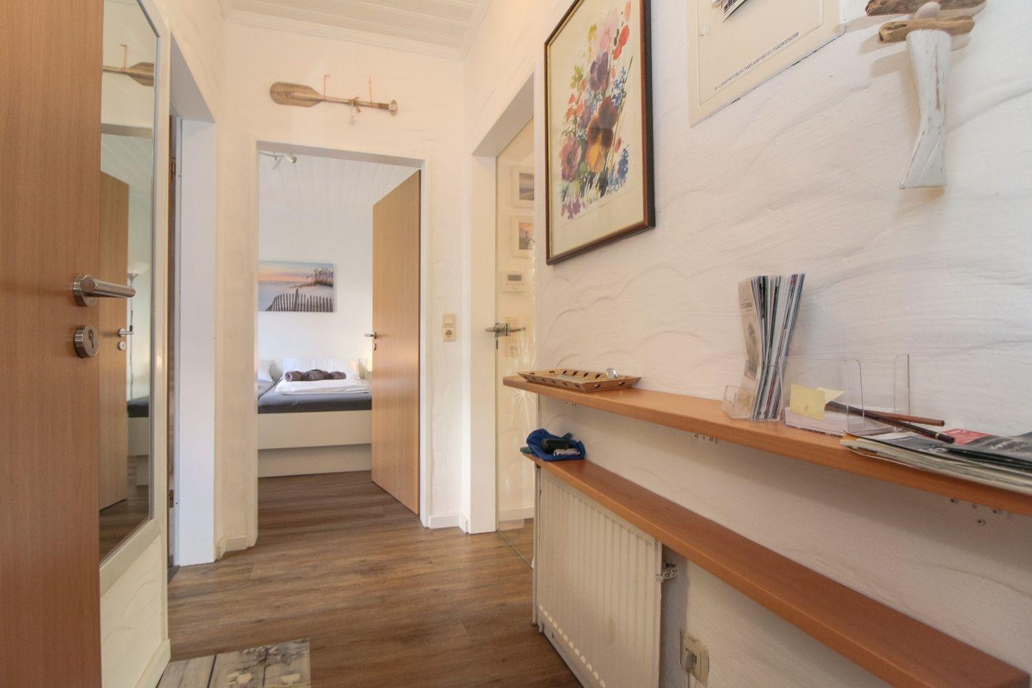 Flur mit Holzdielen, Wandregal und Blick in Schlafzimmer.