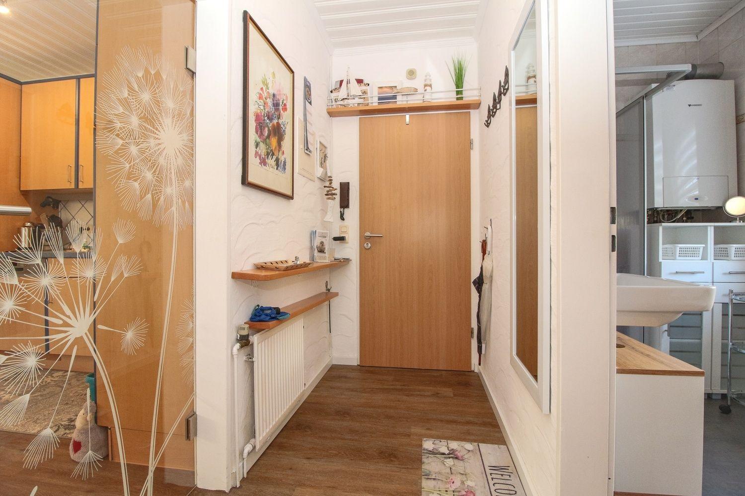 Flur mit Holztür, Wandregalen und Blick in Küche und Bad