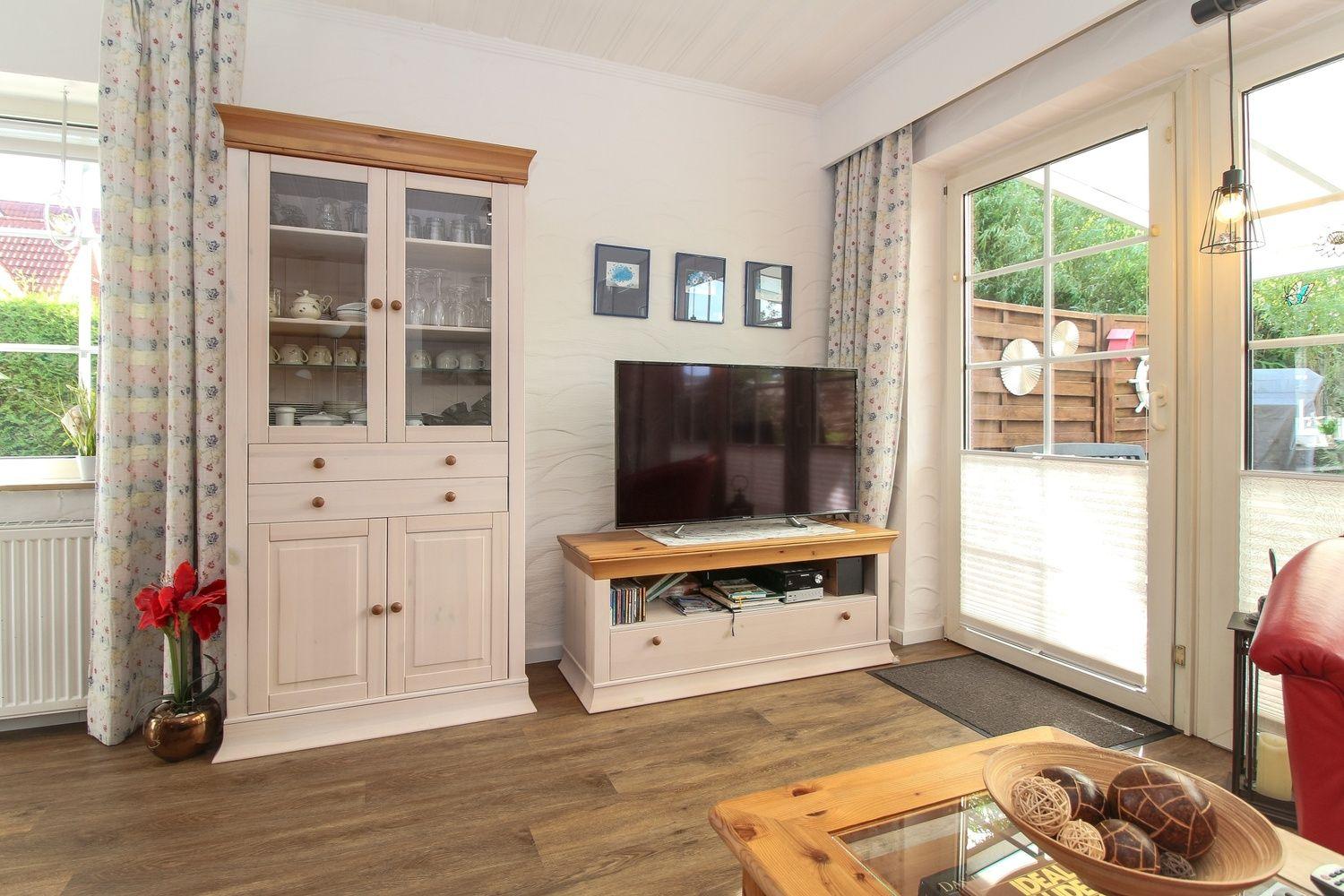 Wohnzimmer mit Fernseher, Schrank und Blick auf den Garten.