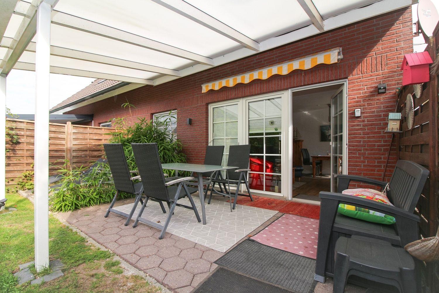 Terrasse mit Tisch, Stühlen und Pavillon. Durchgang in Wohnbereich. Garten mit Pflanzen und Zaun.