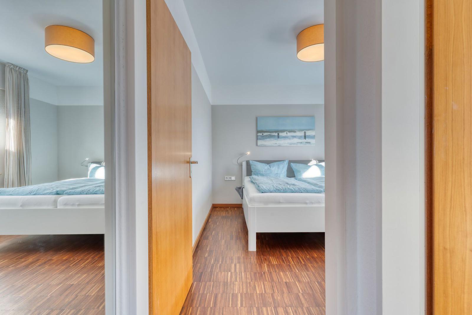 Schlafzimmer mit Bett, Wandbild und Holzboden. Zwei Deckenleuchten sichtbar.