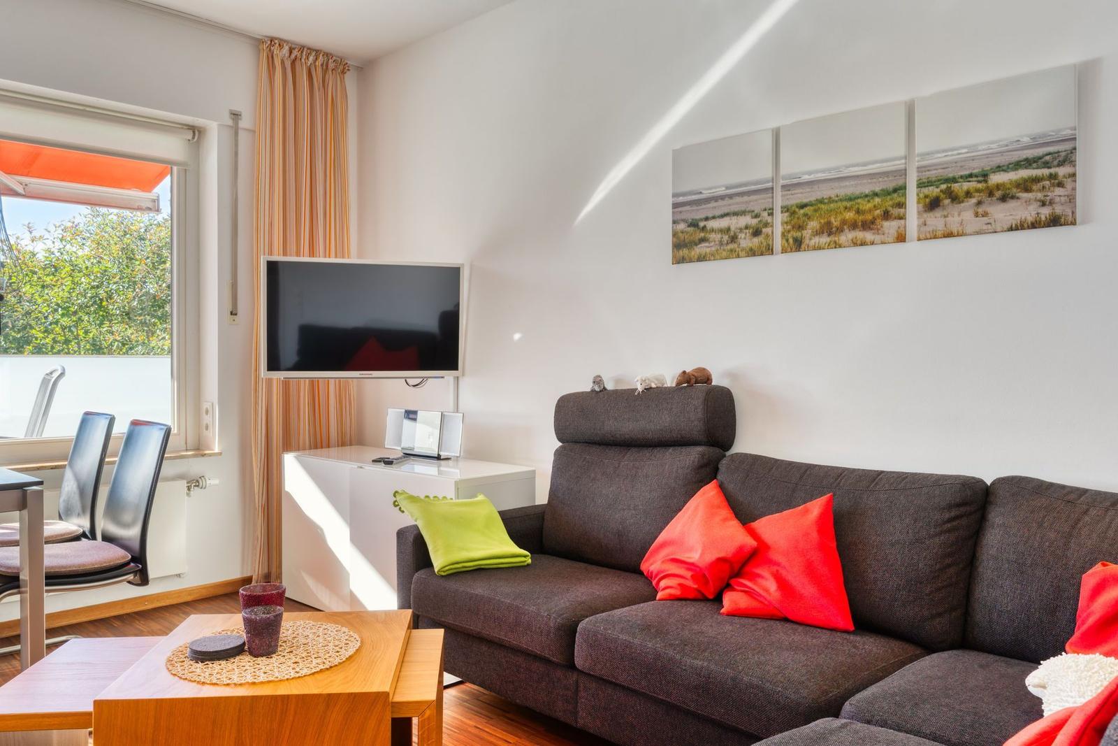 Wohnzimmer mit Sofa, Fernseher und Fenster zum Balkon.