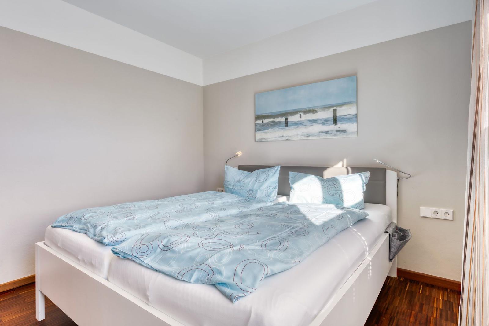 Schlafzimmer mit Bett, Wandbild und Stehlampe.