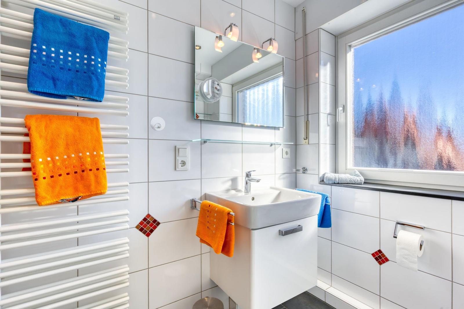 Badezimmer mit Waschbecken, Spiegel und Heizkörper mit Handtüchern.