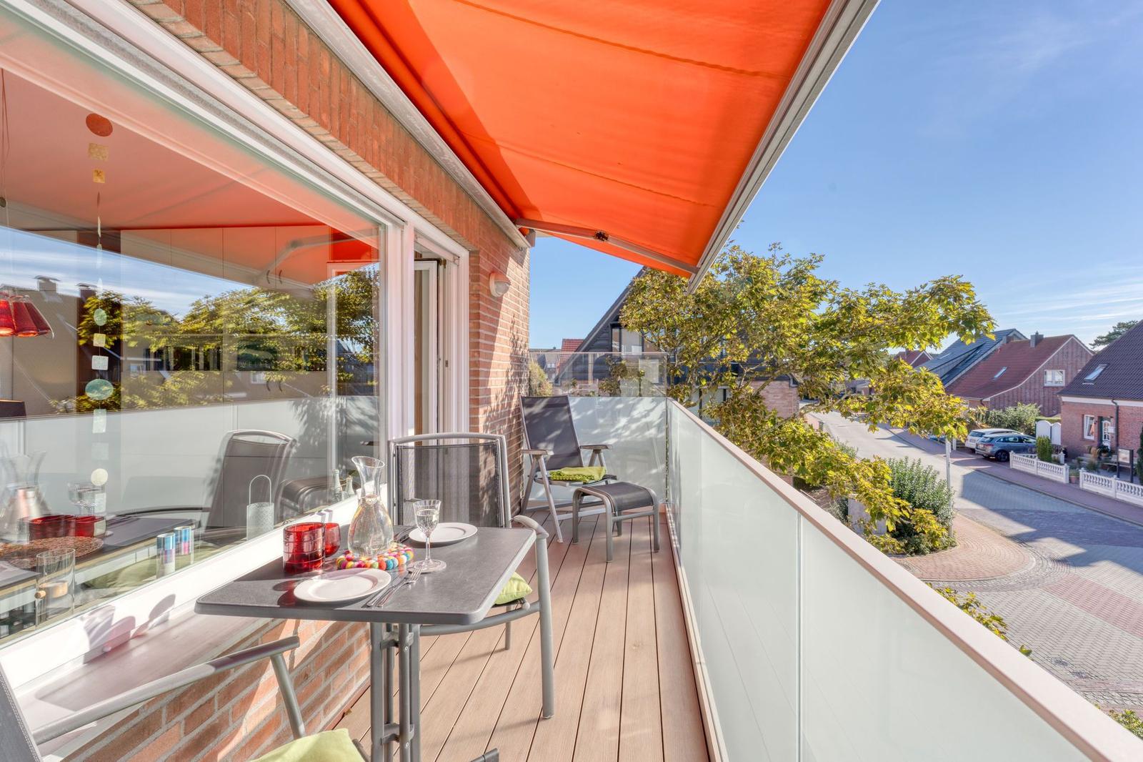 Terrasse mit Tisch, Stühlen und orangefarbenem Markisenüberdachung. Blick auf Straße und Bäume.