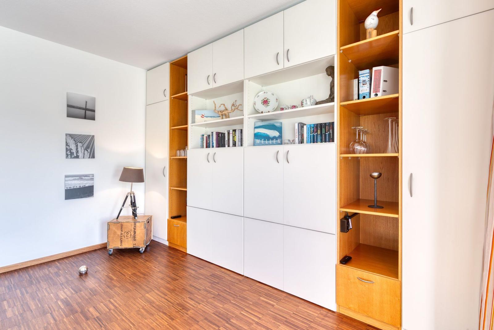 Zimmer mit integriertem Schrank, Wandbildern und Holzboden.