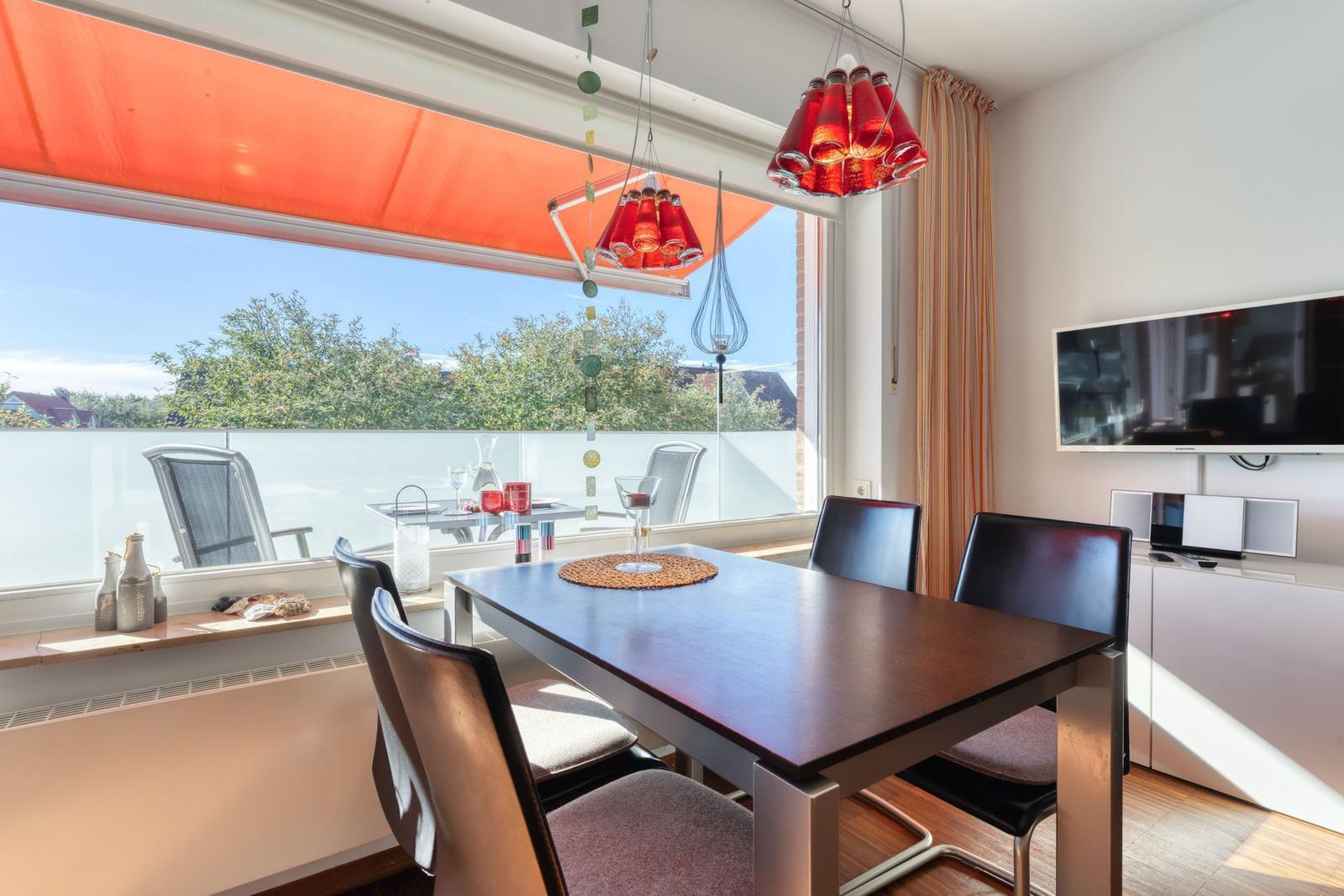 Esszimmer mit Tisch, Stühlen und Balkonansicht. Deckenleuchte und Fernseher.