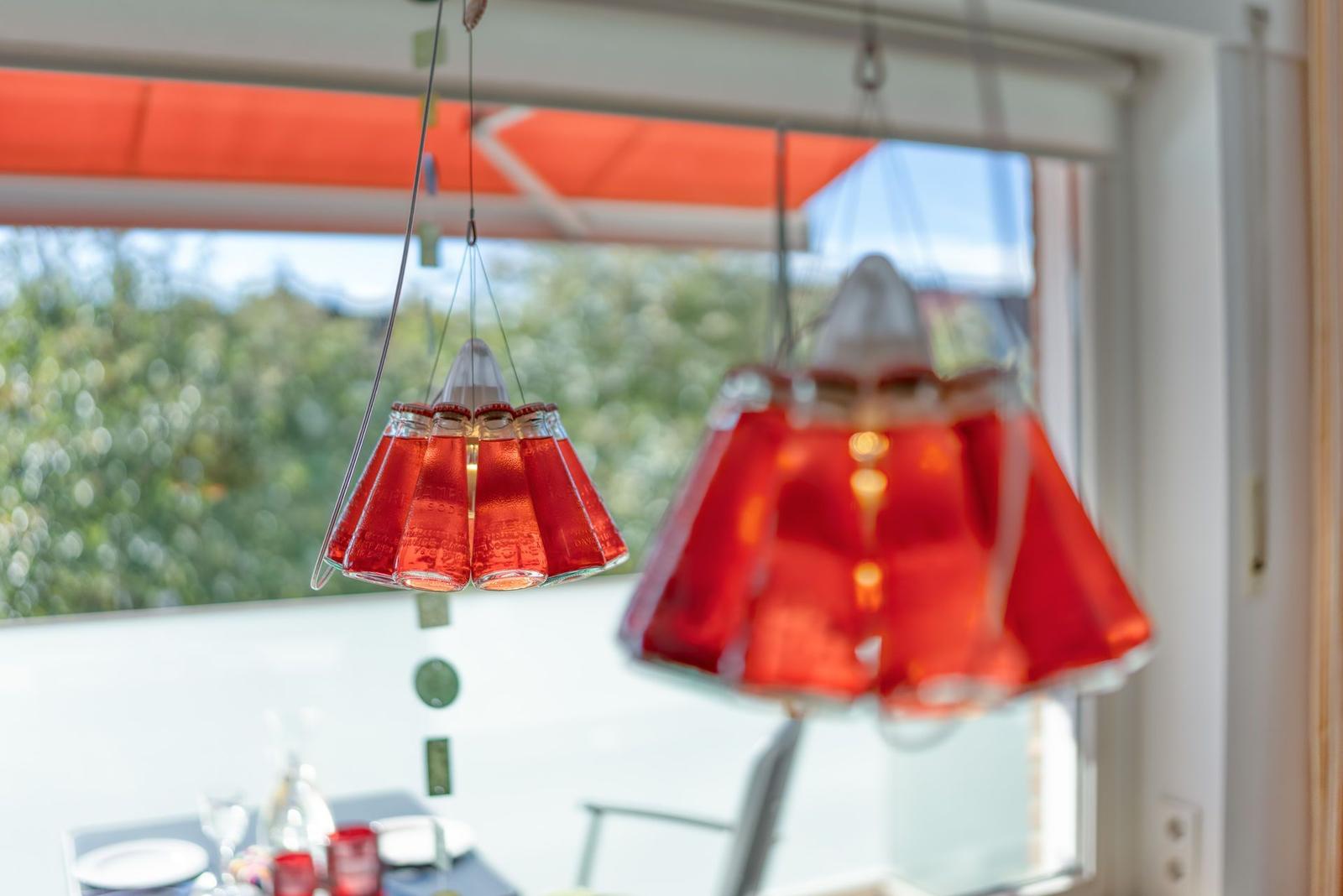Hängende rote Glaslampen über einem Tisch mit Blick auf Balkon und Grün.