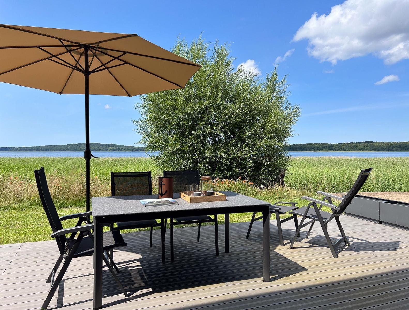 Terrasse mit Tisch, Stühlen und Sonnenschirm am See