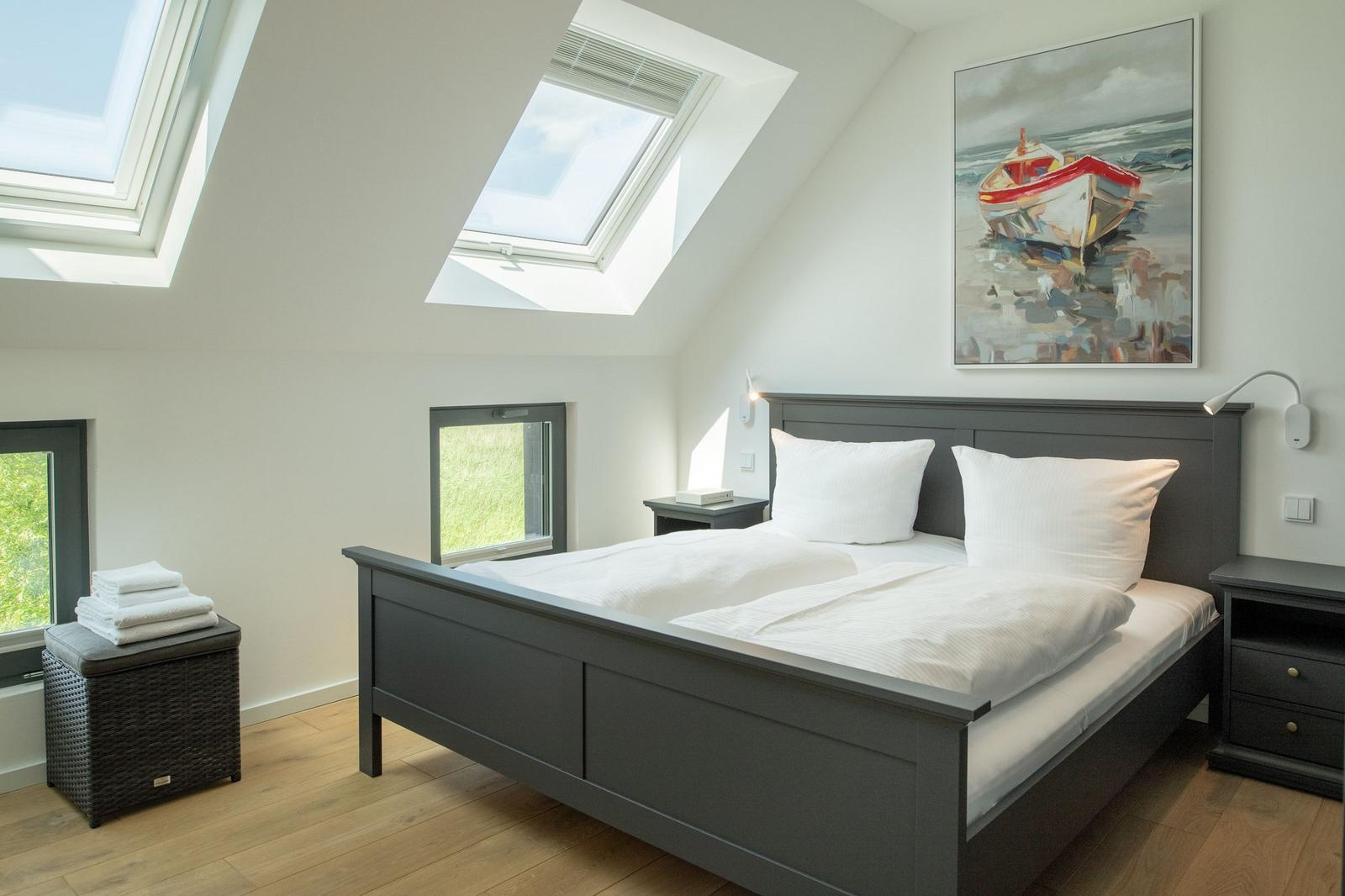 Schlafzimmer mit Dachschrägen, Dachfenstern und Bett mit weißen Kissen.