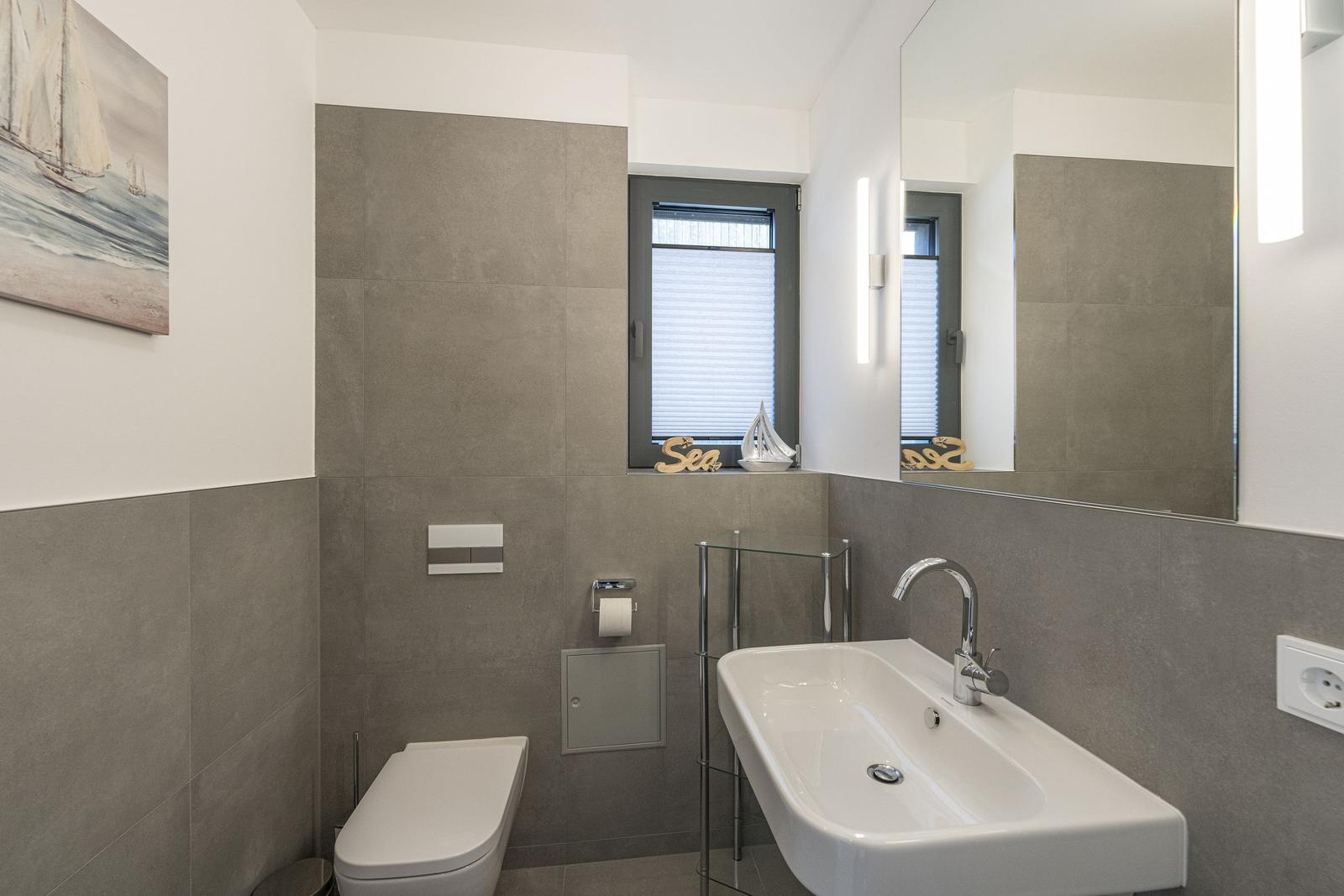 Badezimmer mit Waschbecken, Toilette und Fenster mit Jalousie.