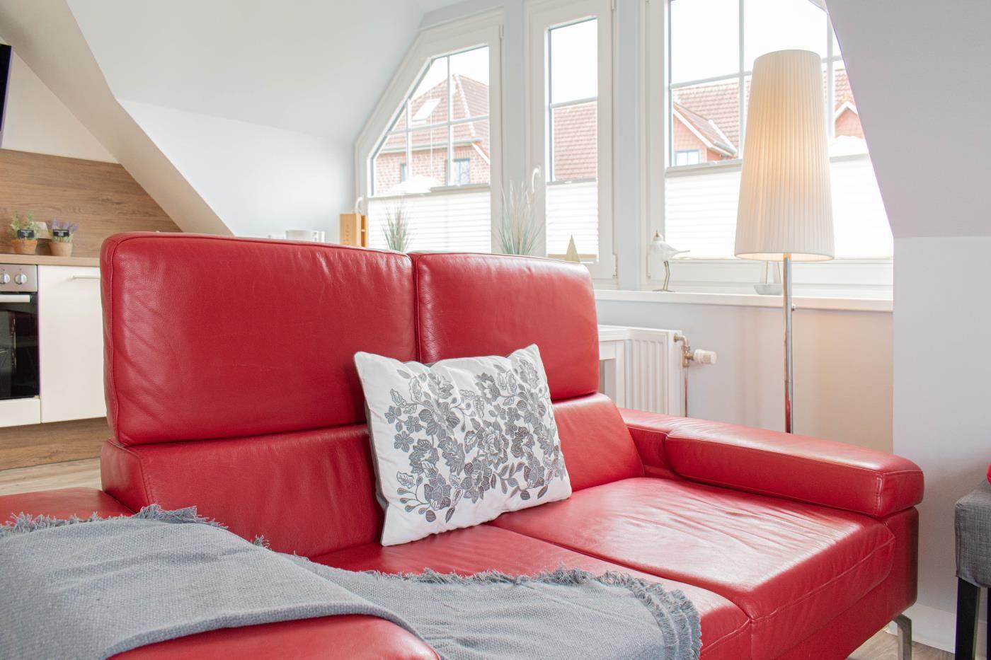 Rotes Sofa mit Kissen und Decke vor Fenster