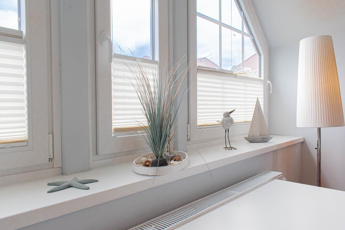 Blick aus dem Fenster mit Blick auf Dächer und Himmel. Auf dem Fensterbrett steht eine Pflanze und Dekoration.