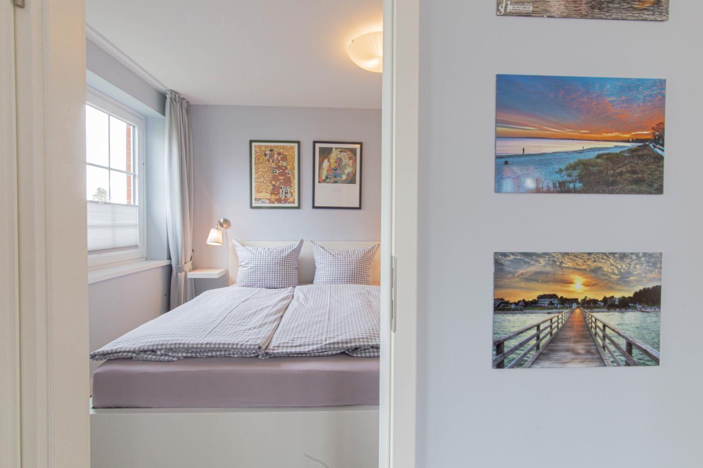 Schlafzimmer mit Doppelbett, Fenster und Wandbildern.