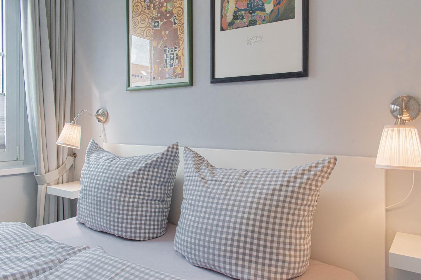 Schlafzimmer mit Bett, Kissen und Wandbildern.