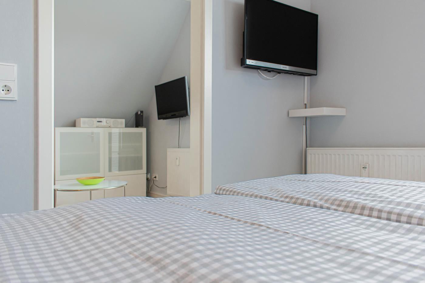 Zimmer mit Bett, Fernseher und Schrank. Decke geneigt. Wandfarbe hellblau.