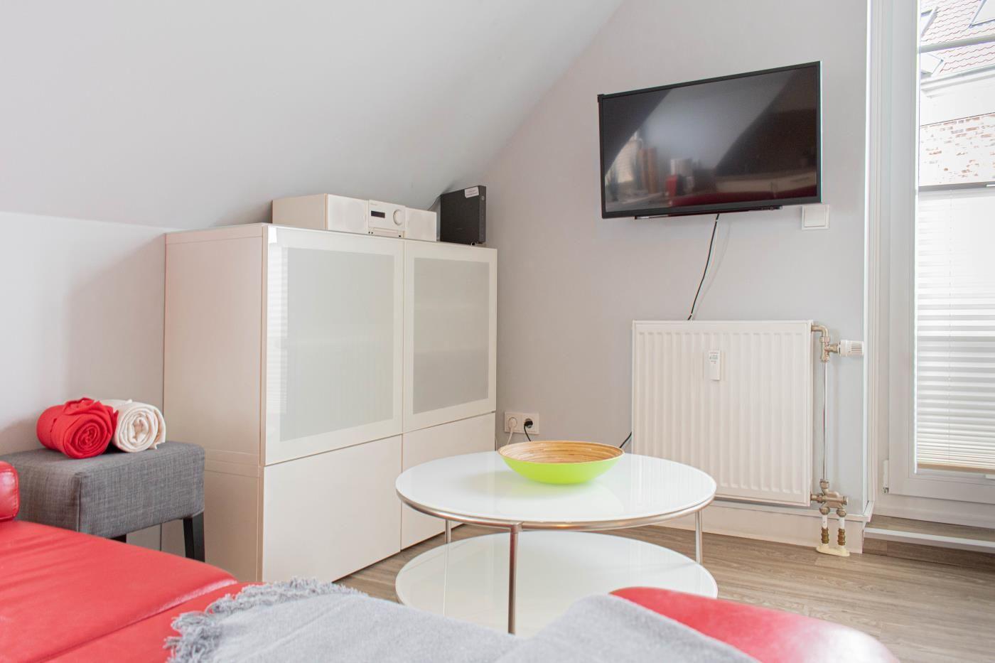 Wohnzimmer mit TV, Couch, Tisch und Fenster.