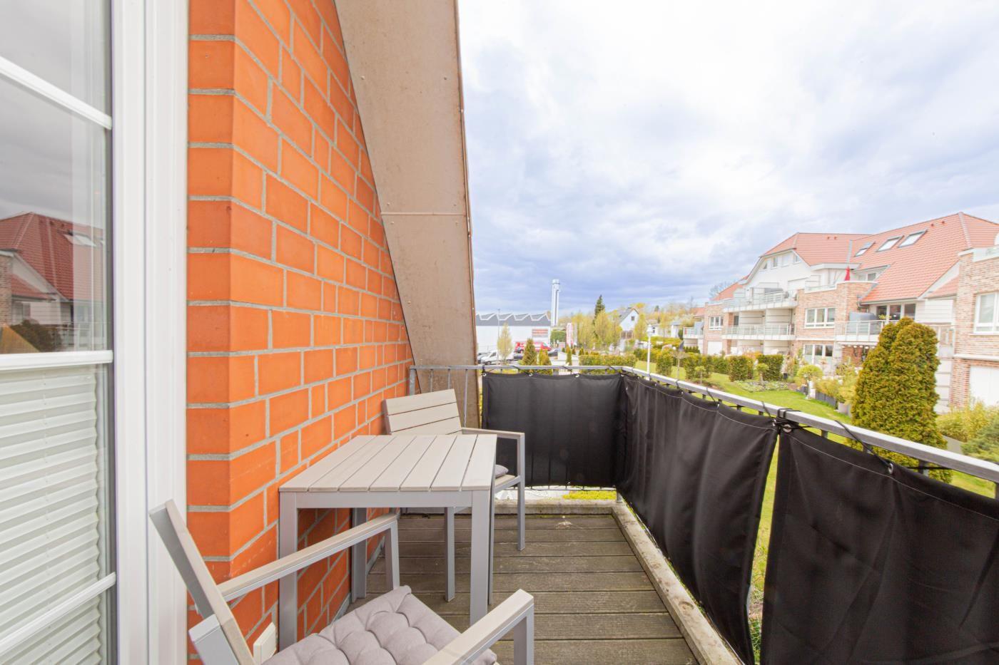 Terrasse mit Tisch und Stühlen, Sicht auf Wohngebiet und Grünflächen.