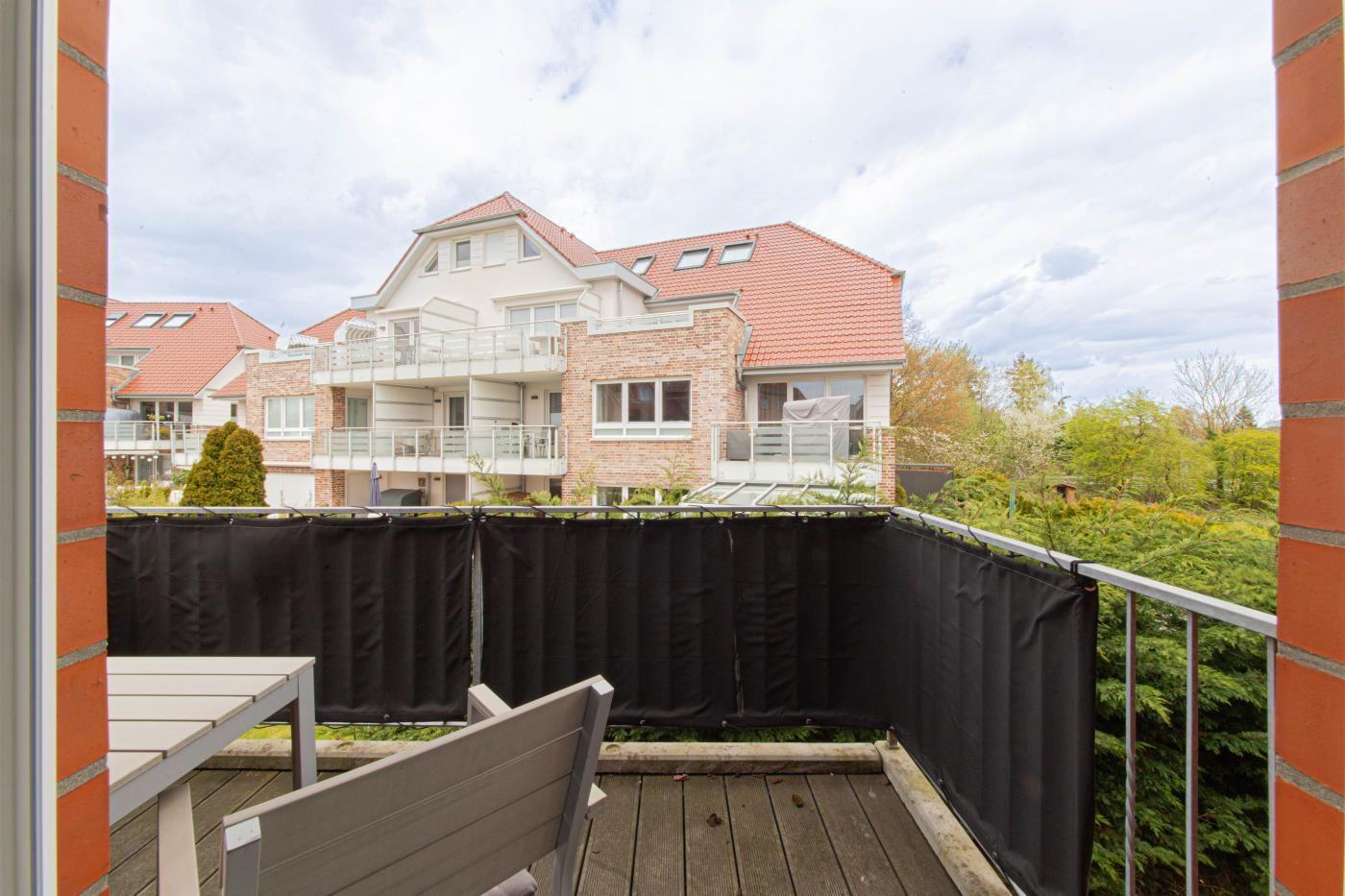 Terrasse mit Tisch und Stühlen, Blick auf Wohnhaus mit Balkon und Garten.