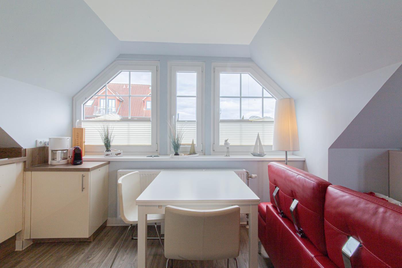 Wohn- und Essbereich mit rotem Sofa, weißem Tisch und Dachfenstern.