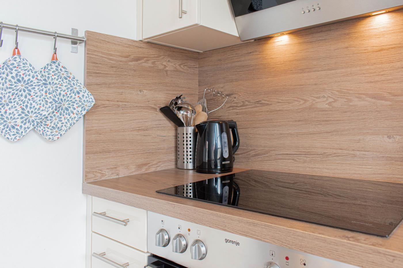 Küche mit Holzrückwand, Kochfeld und Küchengeräten.