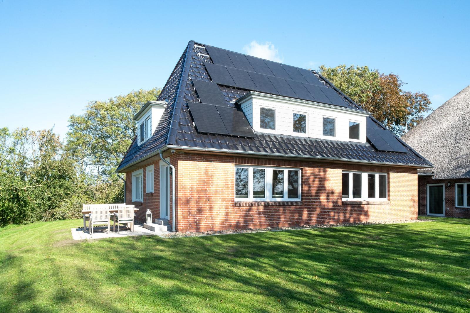 Red brick house with solar panels and terrace in the green.