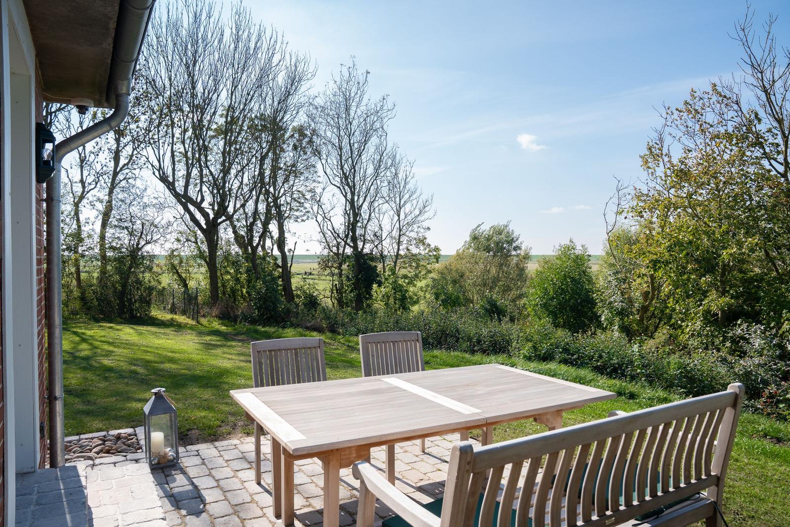Terrace with table and chairs, view of green meadows and trees.