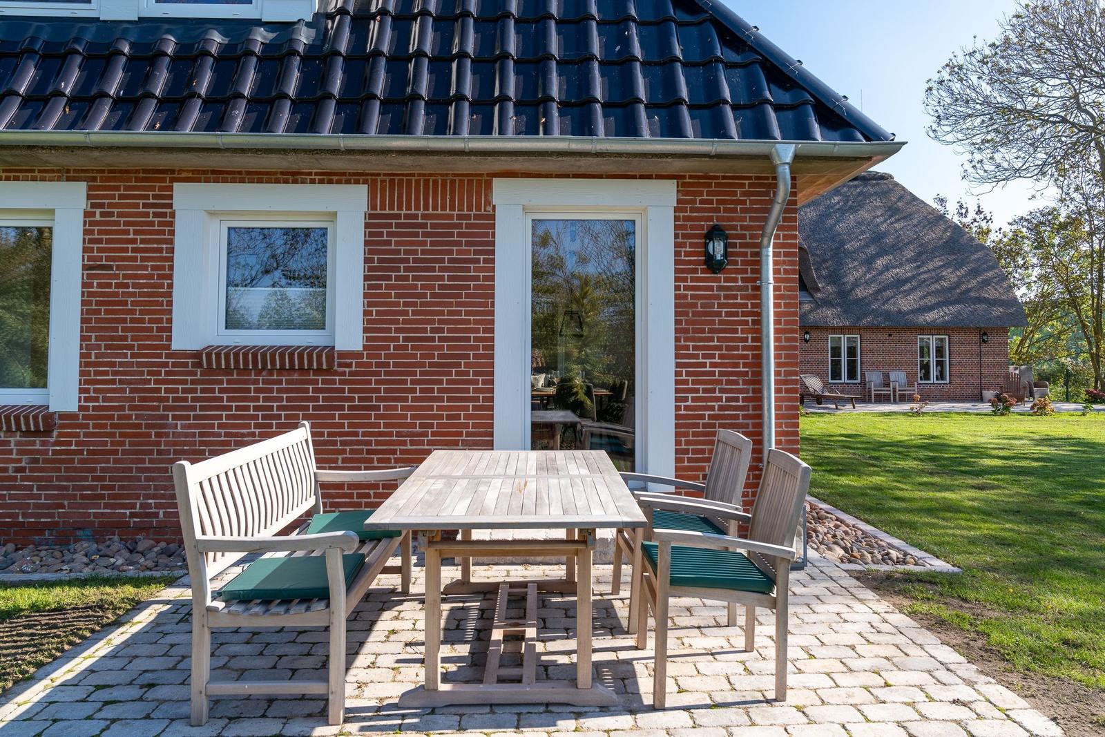 Red brick house with terrace and garden furniture. Courtyard with thatched roof house.