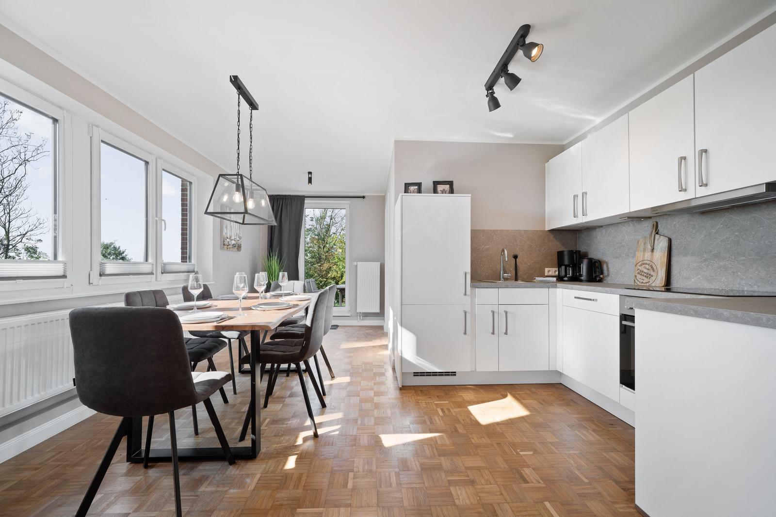 Kitchen and dining area with white built-in kitchen, wooden floor, and large dining table.