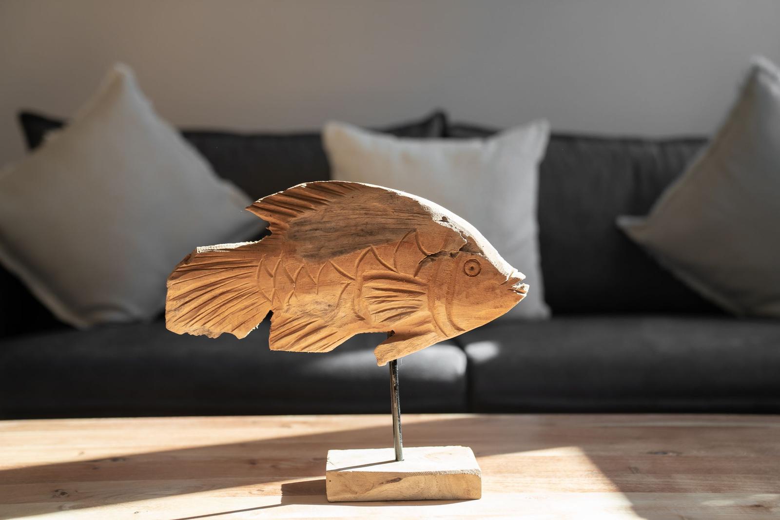 Wooden fish sculpture on table in front of sofa with cushions