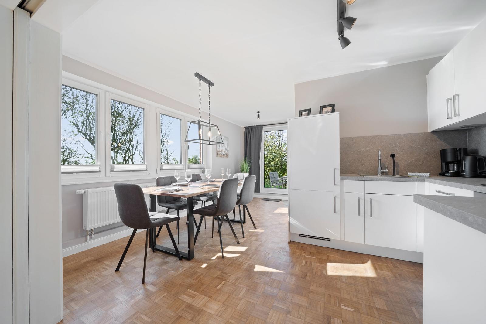 Dining room with table, chairs, and windows. Kitchen with worktop and cabinets.