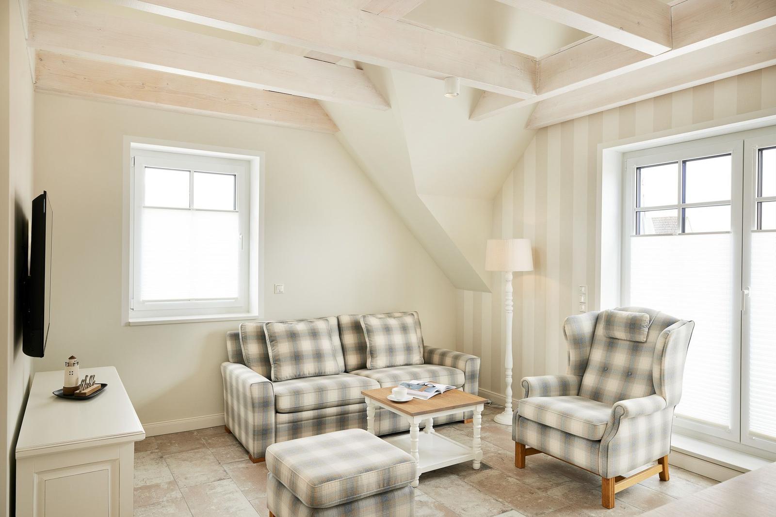 Wohnzimmer mit Sofa, Sessel und TV. Holzbalken an der Decke.