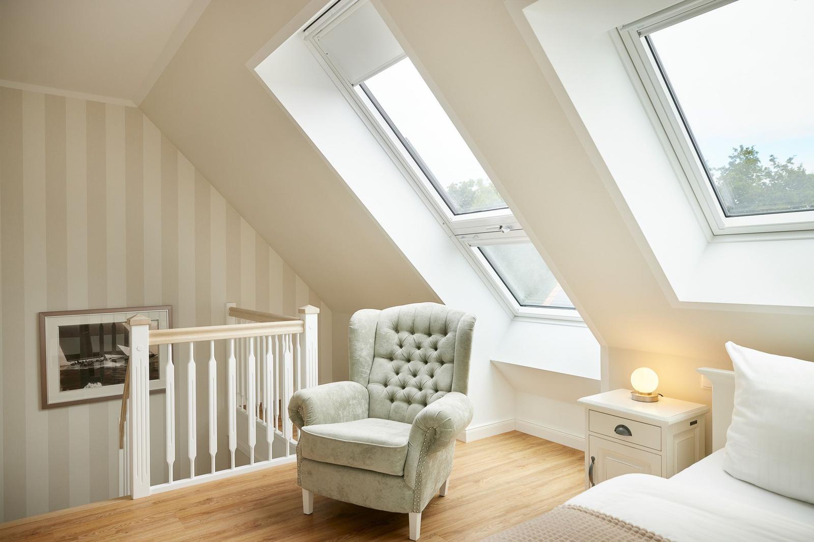 Schlafzimmer mit Dachfenstern, Sessel und Nachttisch.