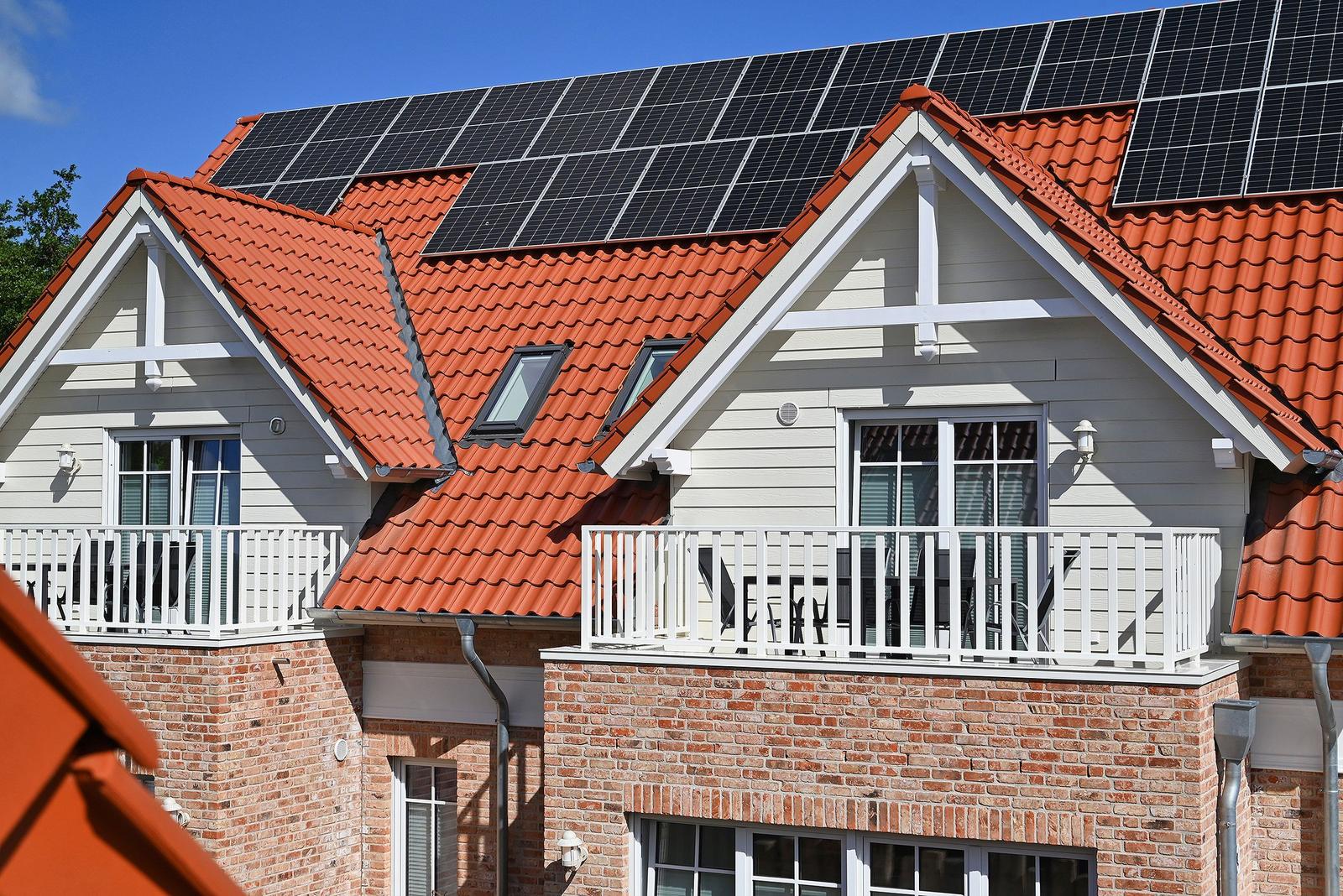 Haus mit Solaranlage, rotem Dach und Balkon mit Tisch und Stühlen.