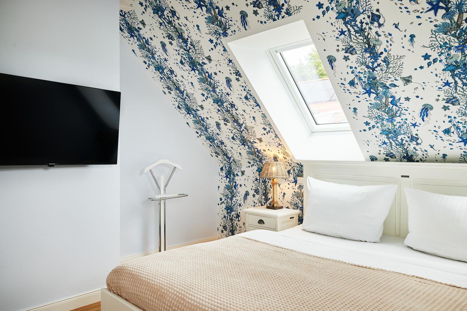 Schlafzimmer mit Dachfenster, blauem Tapetenmuster und Fernseher an der Wand.