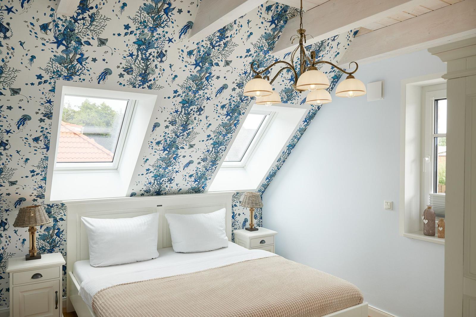 Schlafzimmer mit blauem Muster, Dachfenstern und Bett mit weißen Kissen.