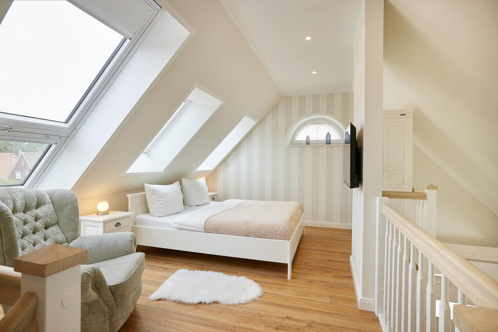 Dachgeschosszimmer mit Bett, Sessel und Dachfenstern.