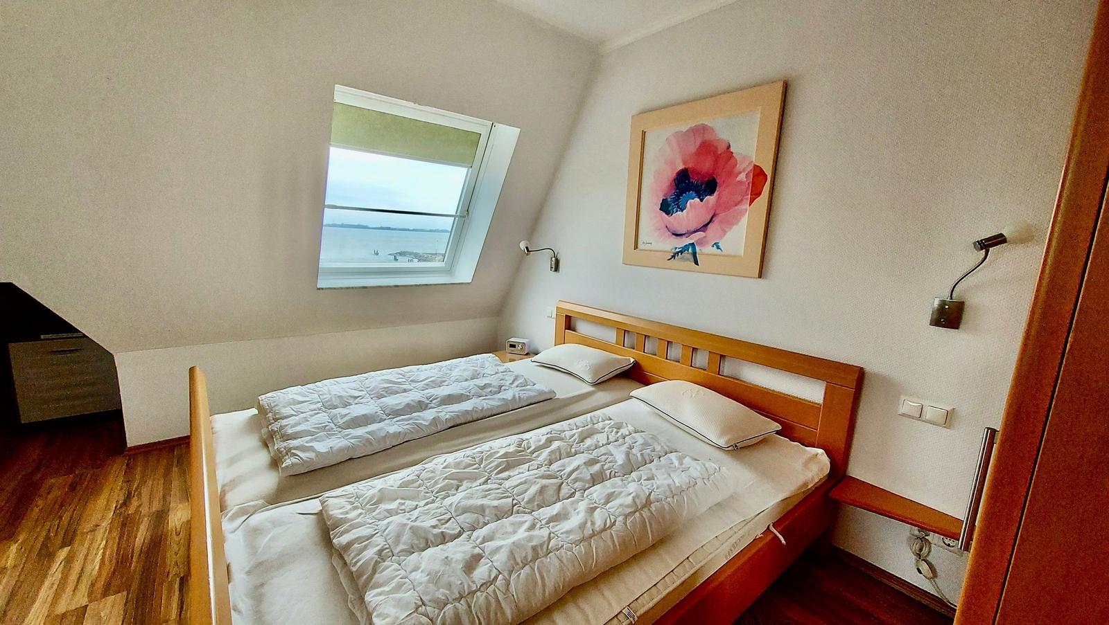 Schlafzimmer mit Doppelbett, Fenster und Wandbild.