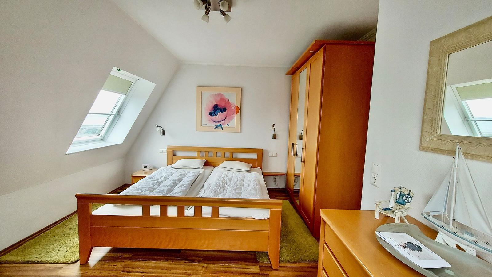 Schlafzimmer mit Dachschrägen, Doppelbett, Kleiderschrank und Fenster.