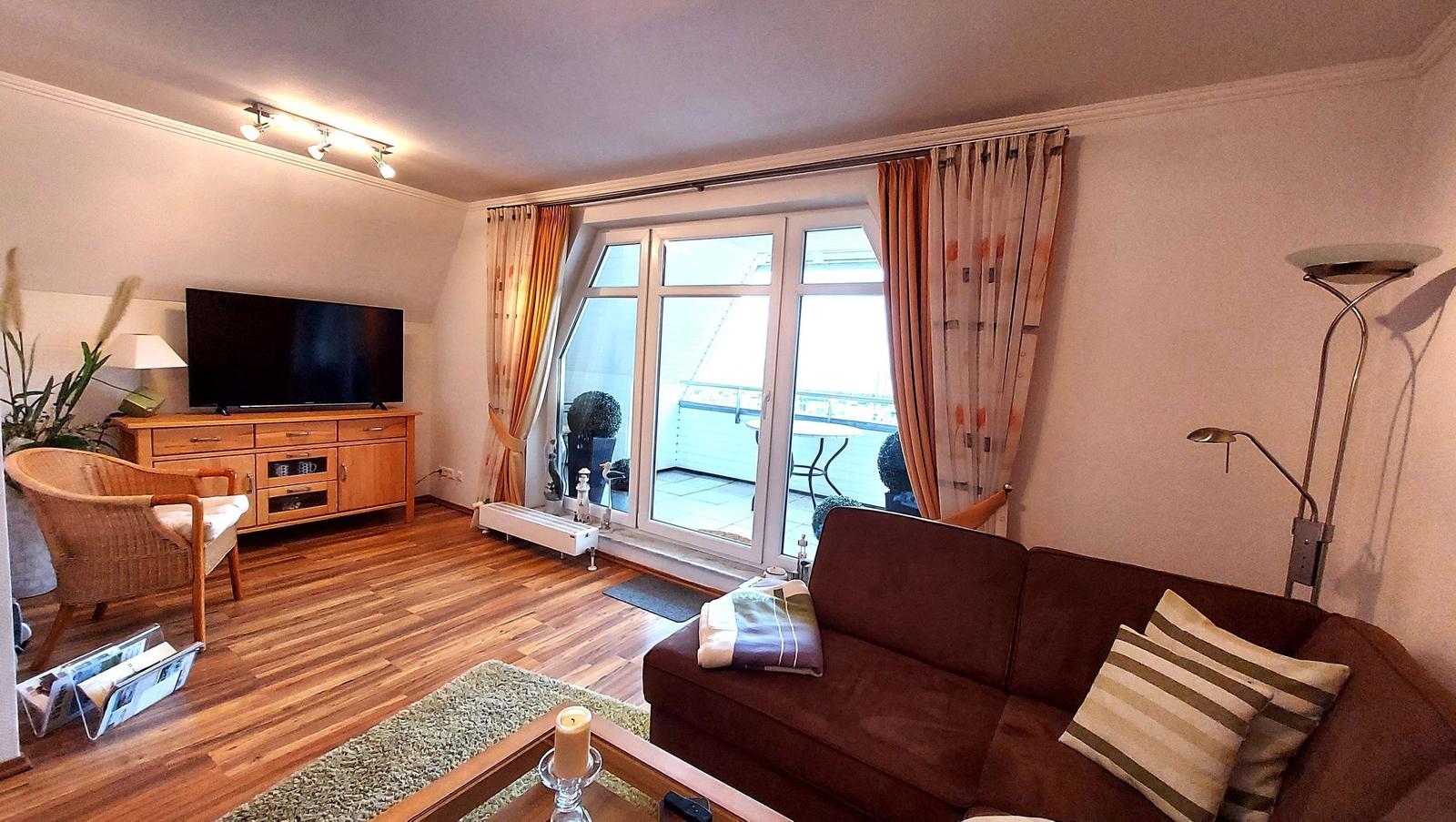 Wohnzimmer mit Sofa, Fernseher und Balkonansicht.