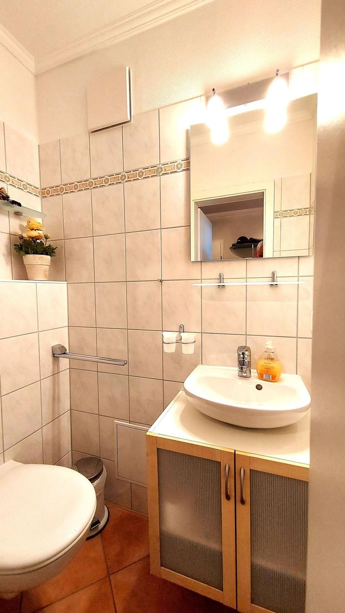 Badezimmer mit Waschbecken, Spiegel, Toilette und Handtuchhalter.