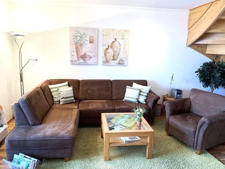 Ein Wohnzimmer mit braunem Sofa, Holz-Tisch und Wandbildern.