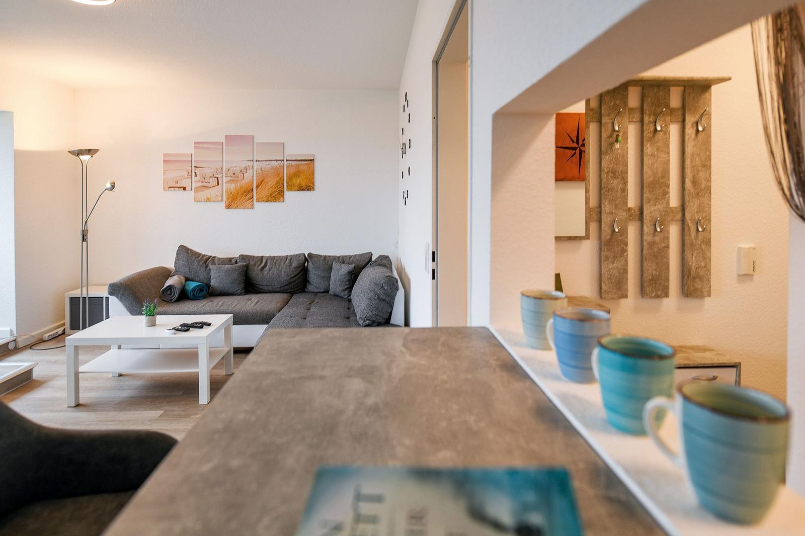 Wohnbereich mit Sofa, Couchtisch und Küchenarbeitsplatte mit Tassen.