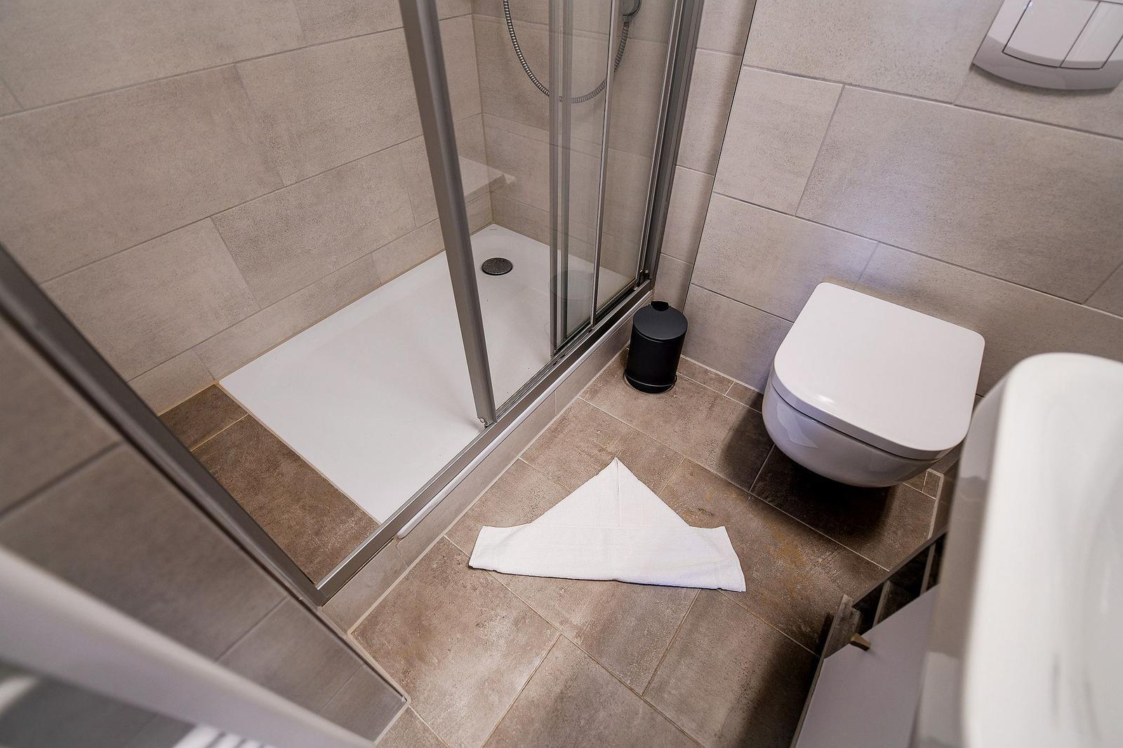 Dusche mit Glaswand, Toilette und Handtuch auf dem Boden.