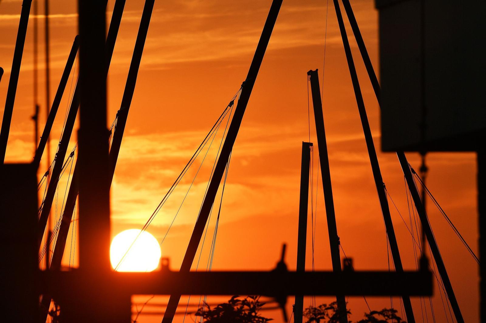 Sonnenuntergang hinter Segelyachten mit Masten und Takelage.