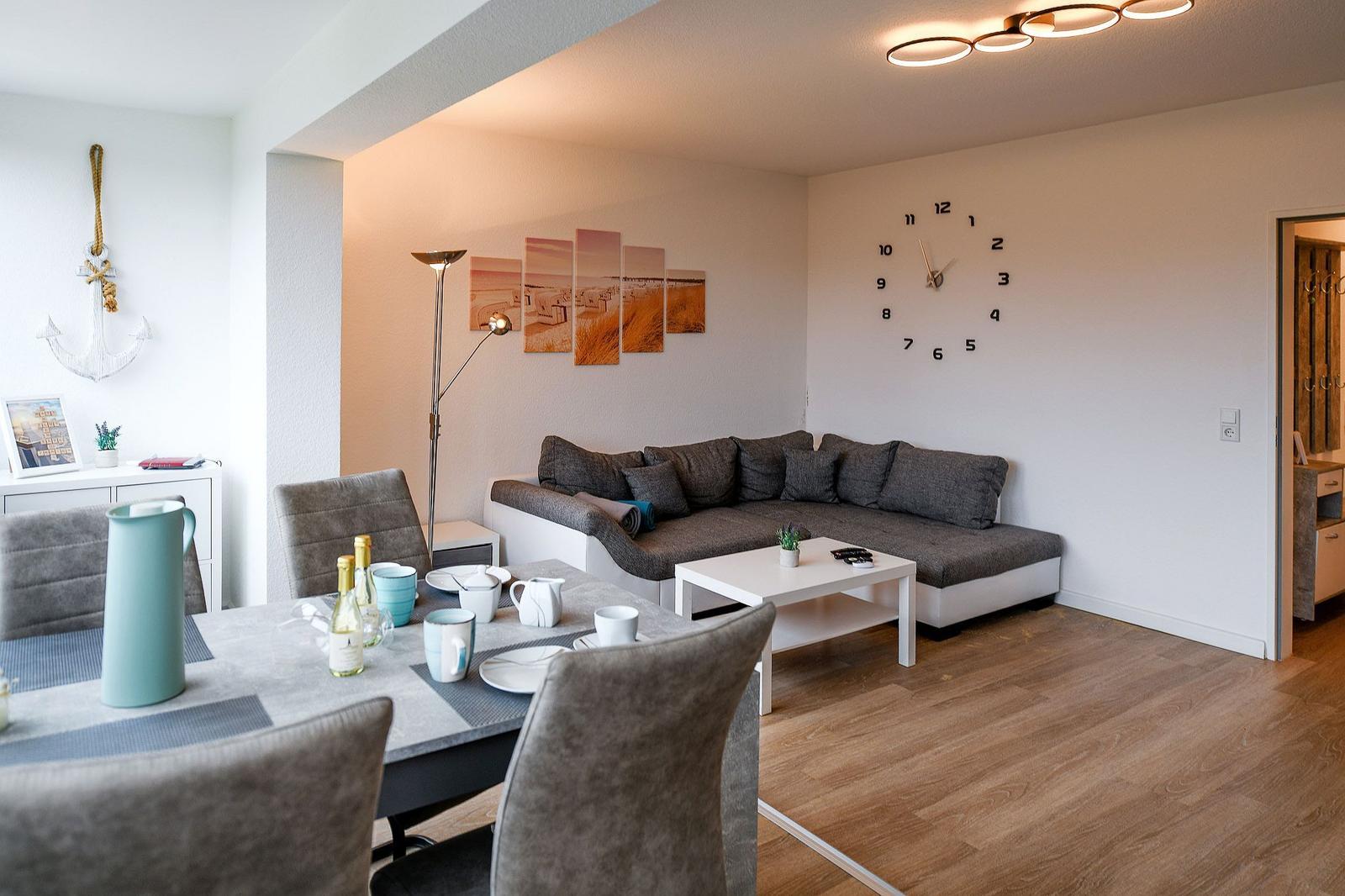 Wohn- und Essbereich mit Sofa, Tisch und Wanduhr.