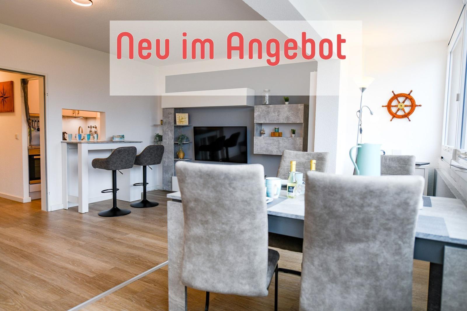 Wohnbereich mit Esstisch, TV und Küchenbereich. Holzfußboden und helles Ambiente.